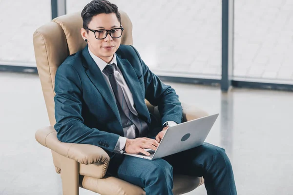スーツと眼鏡のラップトップを使用して オフィスでカメラ目線でハンサムな青年実業家のハイアングル — ストック写真