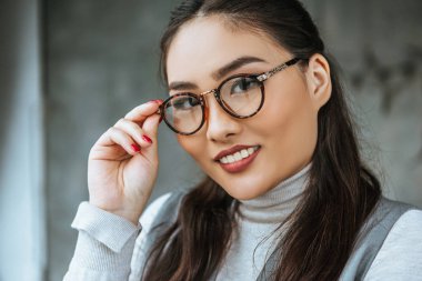 yakın çekim gözlük ayarlama ve kameraya gülümseyen güzel Asya işkadını portresi