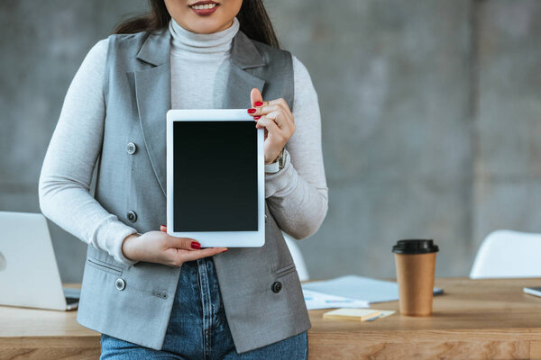 cropped shot of smiling businesswoman holding digital tablet with blank screen in office