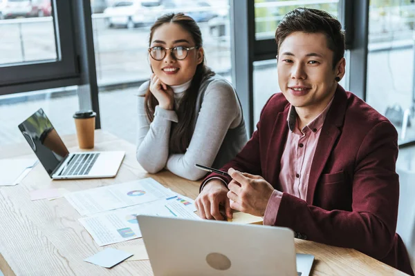 Glade Unge Asiatiske Forretningsfolk Som Jobber Med Bærbare Datamaskiner Smiler – stockfoto