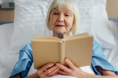 üst düzey kadın yatakta yatan ve hastanede kitap okuma