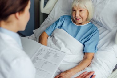 tanı tutarak ve gülümseyen hastane yatağında yalan üst düzey kadın danışmanlık doktor 