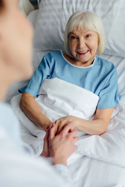 女医生与快乐的老年妇女牵手躺在医院的床上 — 图库照片