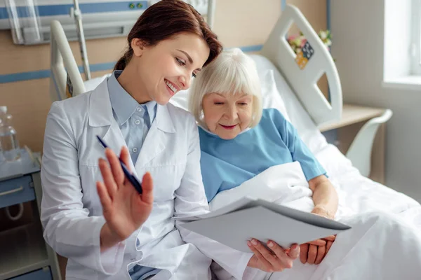 Feliz Médico Mujer Sosteniendo Diagnóstico Consultando Mujer Mayor Acostada Cama — Foto de Stock