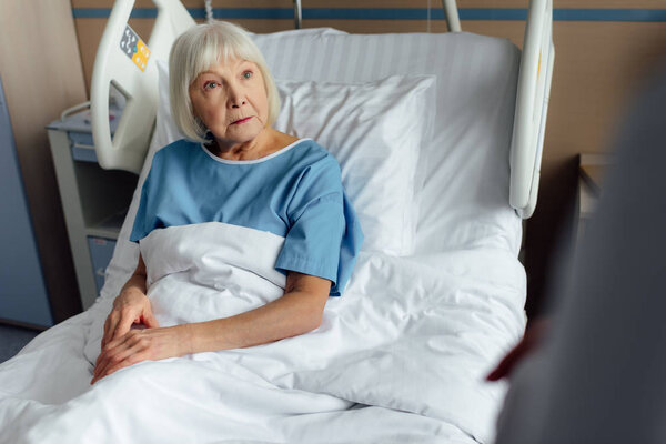 selective focus of sad senior woman with grey hair lying in hospital bed