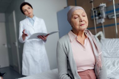 atkı kanseri tanı arka planda tutan kadın doktor ile hastane yatağı üzerinde oturan üzgün üst düzey kadın