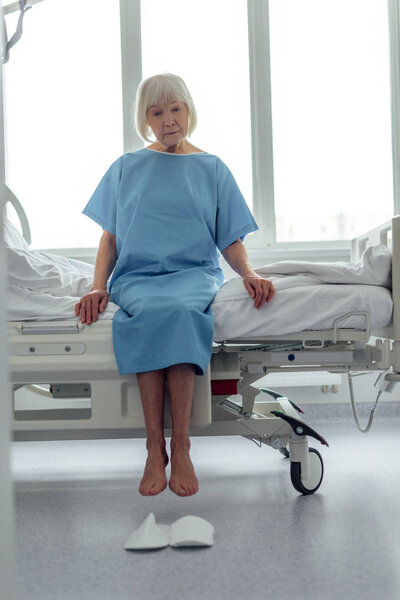 sad senior woman sitting on bed in hospital ward 