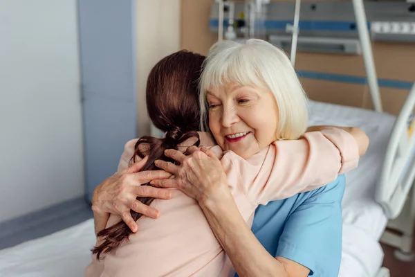 快乐的老年妇女和女儿坐在床上 拥抱在医院 — 图库照片