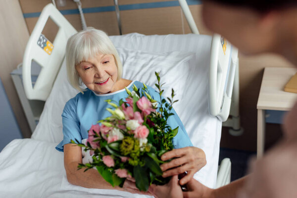 daughter presenting flowers to happy senior woman in hospital