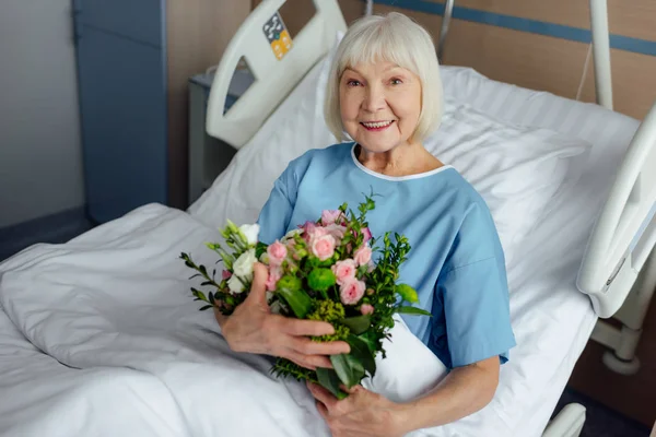 Счастливая Выздоравливающая Пожилая Женщина Лежит Постели Цветами Смотрит Камеру Больнице — стоковое фото