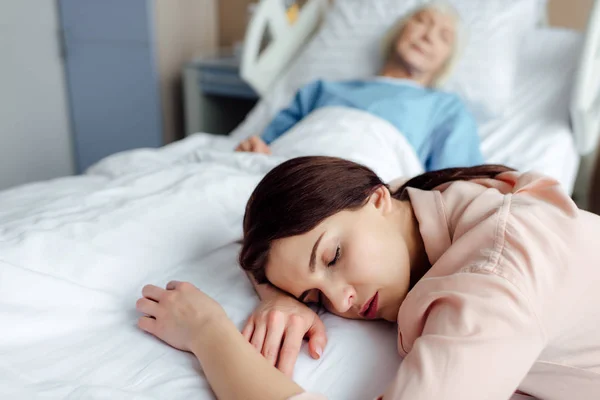 病院の背景のベッドで病気の母親に疲れて眠っている娘の選択と集中 — ストック写真