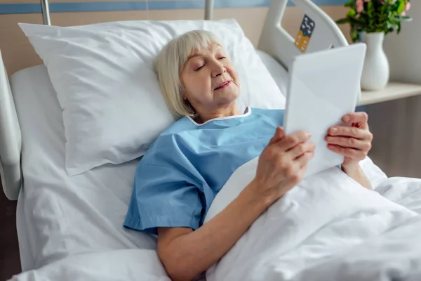 老年妇女躺在床上 在医院使用数字平板电脑 — 图库照片
