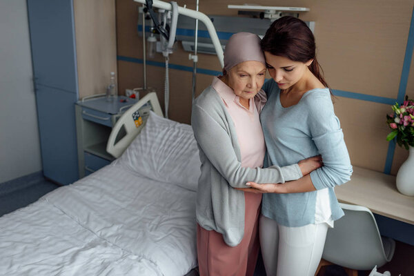 upset daughter embracing sick senior mother with cancer in hospital