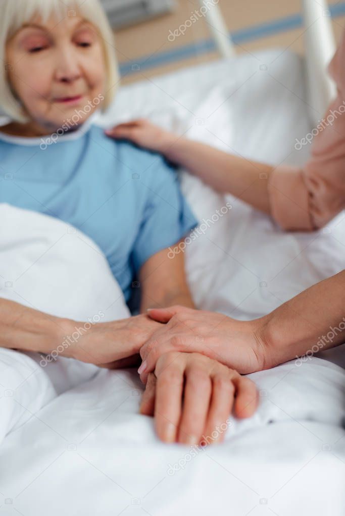 selective focus of senior woman and daughter holding hands in hospital