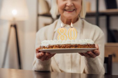 Doğum günü pastası ile sayı 80 üstüne evde tutan gülümseyen kadın kıdemli görünümünü kırpılmış 