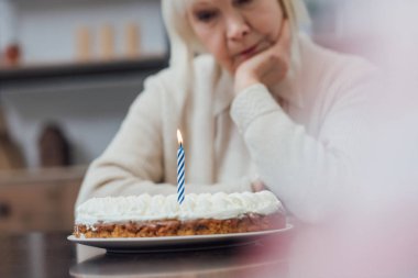 seçici odak masada oturan ve evde mum yanan ile Doğum günü pastası seyir üzgün üst düzey kadın