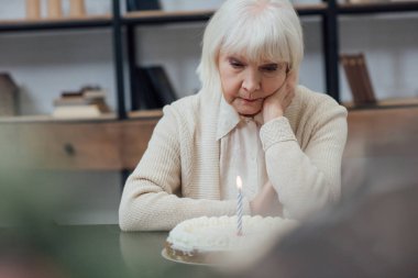 masada oturan ve evde mum yanan ile Doğum günü pastası arayan yalnız üst düzey kadın