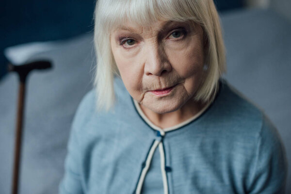 portrait of sad senior woman with grey hair looking at camera at home