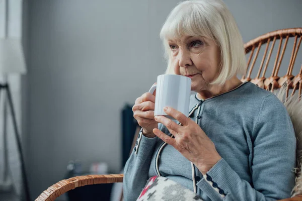 籐ロッキングチェアに座っていると 家でコーヒーを飲む年配の女性 — ストック写真