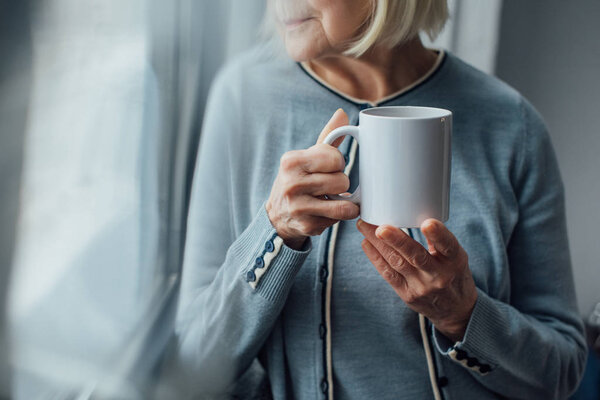 cropped view of senior woman holding cup of coffee at home 