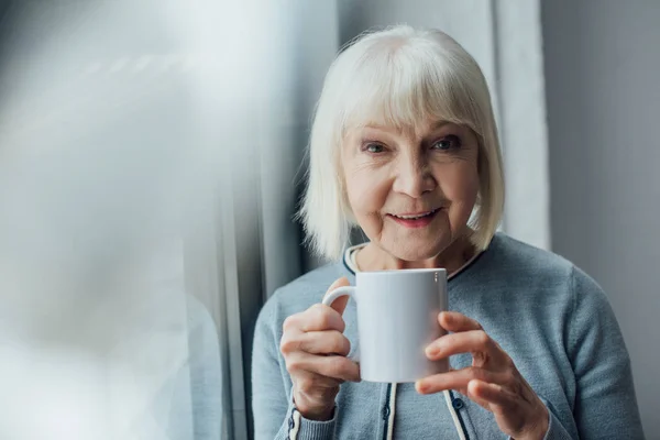 Sorrindo Mulher Idosa Segurando Xícara Café Casa Olhando Para Câmera — Fotografia de Stock