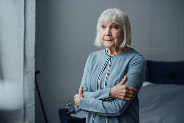 thoughtful senior woman in casual sweater with arms crossed at home