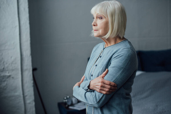 pensive senior woman in casual sweater with arms crossed at home