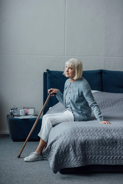 Mulher Sênior Olhando Para Longe Sentado Cama Com Bengala Casa — Fotografia de Stock