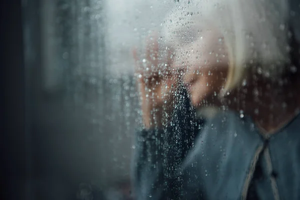 Размытый Портрет Одинокой Пожилой Женщины Дома Через Окно Капельками Дождя — стоковое фото