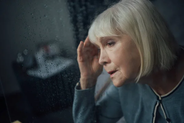 悲伤的老年妇女的肖像 在家里头痛通过窗口与雨滴 — 图库照片