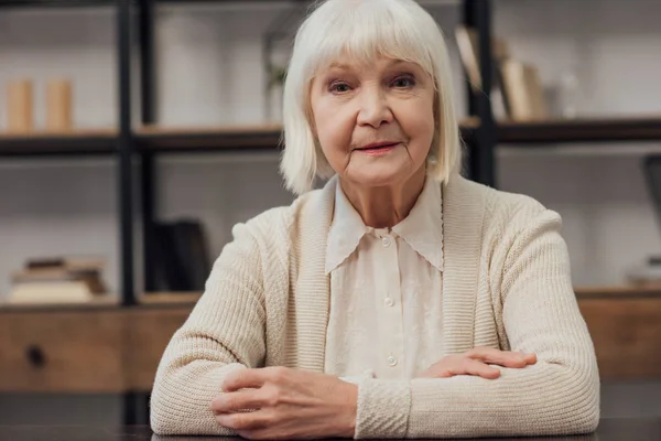 Senior Vrouw Met Grijze Haren Gevouwen Handen Zitten Kijken Camera — Stockfoto