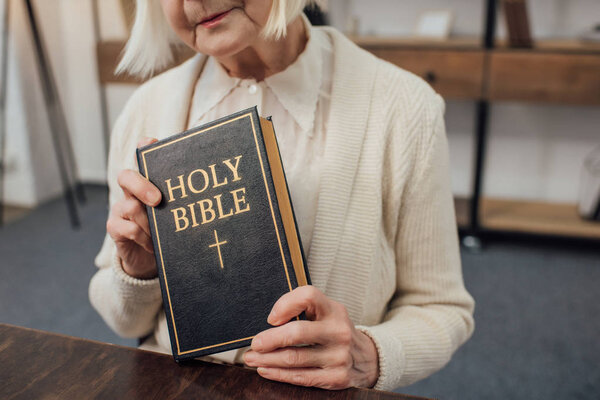 cropped view of senior woman holding holy bible at home