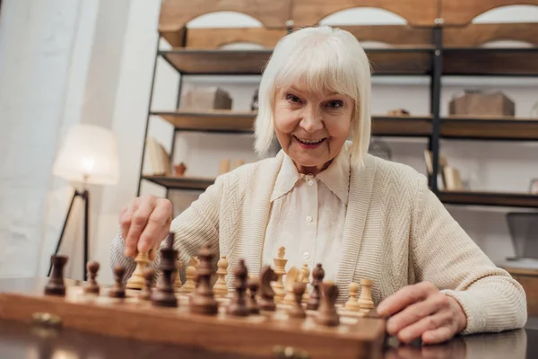 Mujer Mayor Sonriente Sentada Mesa Mirando Cámara Jugando Ajedrez Casa — Foto de Stock