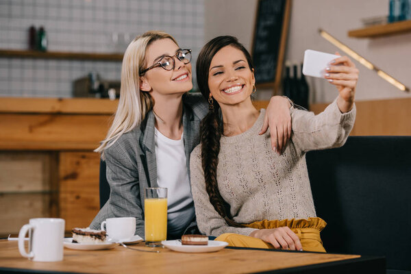 happy women smiling while taking selfie in cafe