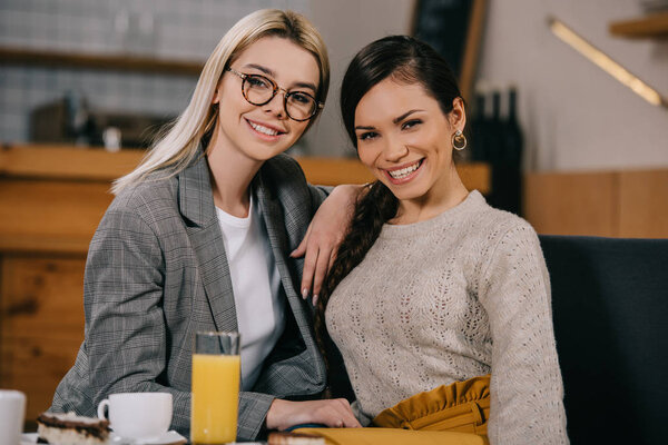 cheerful woman sitting with friend in glasses in cafe