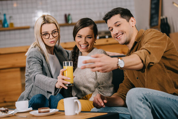 handsome man taking selfie with female friends in cafe