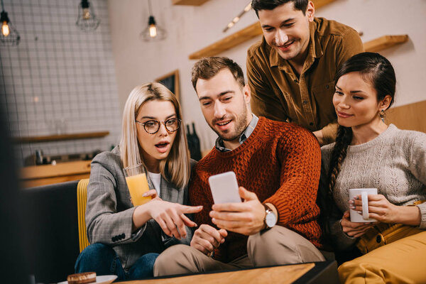 surprised woman in glasses pointing with finger at smartphone while holding drink