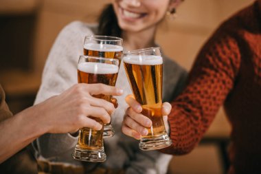 cropped view of happy friends clinking with beer