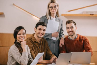 group of happy coworkers smiling in cafe near gadgets clipart