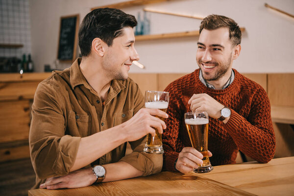 cheerful friends smiling while holding glasses with beer 