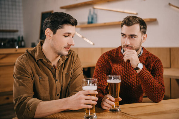handsome man looking at glass of beer near friend