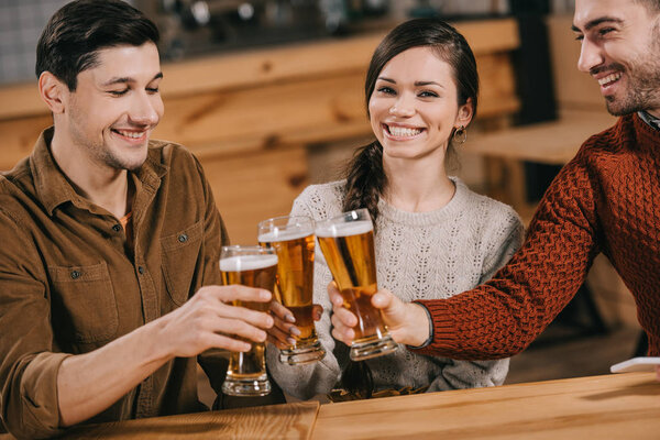happy woman smiling near friends while clinking with beer 