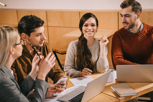 веселая женщина сидит рядом с коллегами в кафе
 