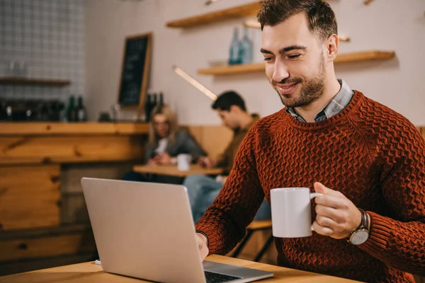 カフェでのコーヒーのカップを押しながらノート パソコンを見て陽気な男 — ストック写真