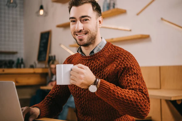 Homem Bonito Segurando Copo Com Bebida Perto Laptop Café — Fotografia de Stock