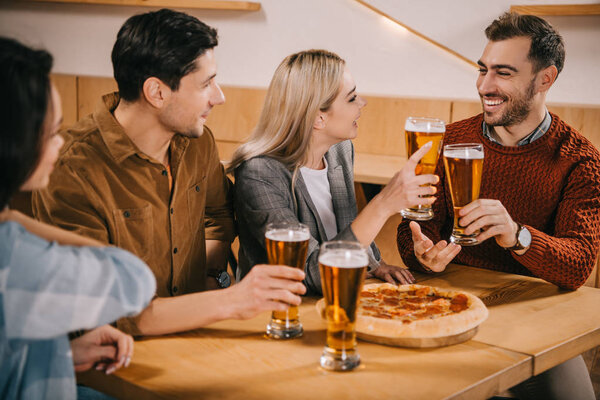 selective focus of cheerful friends toasting glasses of beer in bar