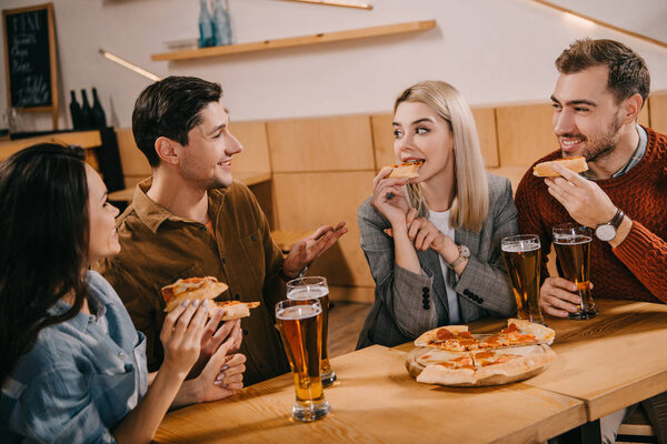 cheerful woman eating pizza near friends in bar