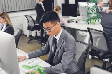 kağıtları ve Office masaüstü bilgisayar çalışma odaklı genç Asya iş adamı yüksek açılı görünüş