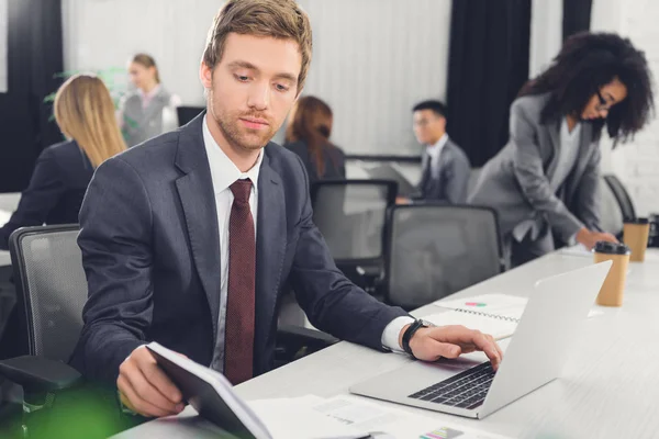 Ernstige Jonge Zakenman Holding Notitieboekje Laptop Gebruiken Office — Stockfoto