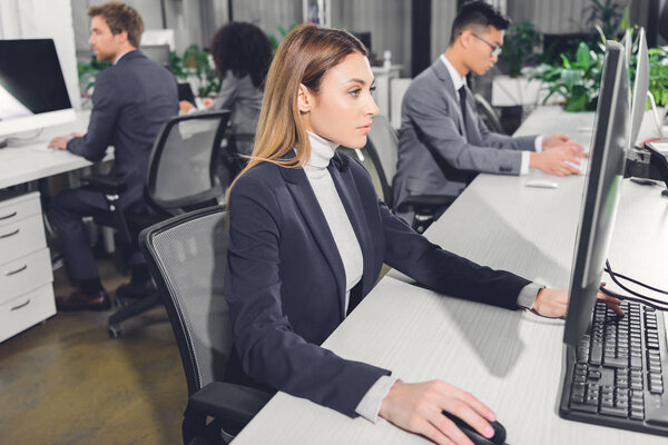 focused young businesswoman using desktop computer while working with colleagues in open space office
